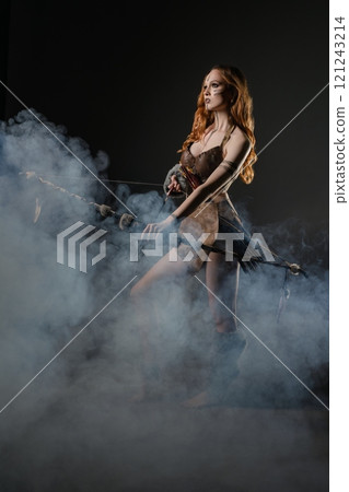 A young woman in a mystical costume walks through smoke-filled darkness 121243214