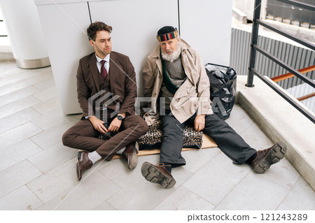 Top view of business man in suit and old homeless male sitting on piece of cardboard on ground, symbolizing social inequality and economic disparity. Concept of social issues and poverty. 121243289