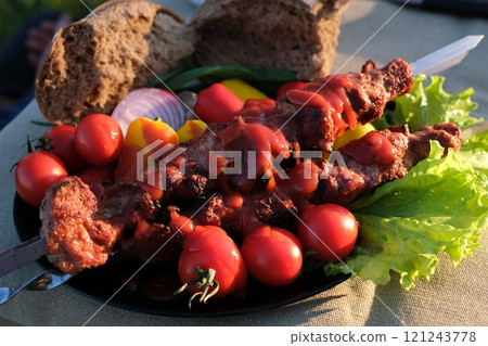 Close-up Adana kebab grilling with vegetables on barbecue charcoal grill. Smoke rising above traditional Turkish kebab grilled on skewers 121243778
