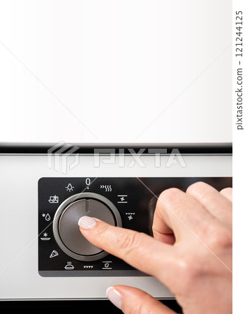 Woman adjusting modern white oven in kitchen.  Female hand pushing and turning knobs on oven control panel 121244125