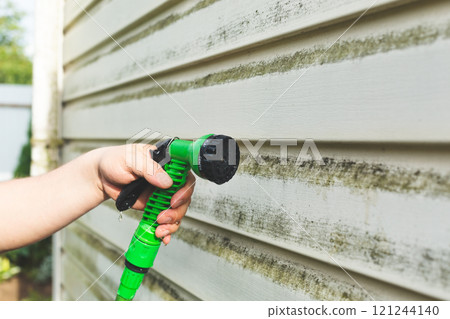Cleaning algae and mold from vinyl siding of house with brush 121244140