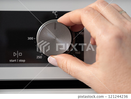 Woman adjusting modern white oven in kitchen.  Female hand pushing and turning knobs on oven control panel 121244236