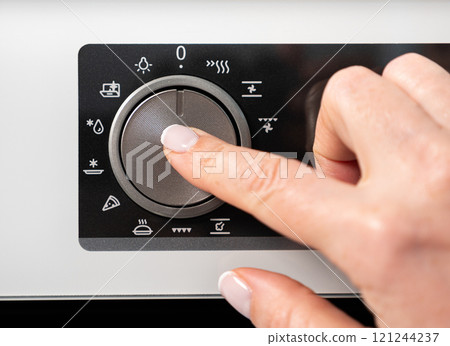Woman adjusting modern white oven in kitchen. Female hand pushing and turning knobs on oven control panel Woman adjusting modern white oven in kitchen. Female hand pushing and turning knobs on oven control panel 121244237