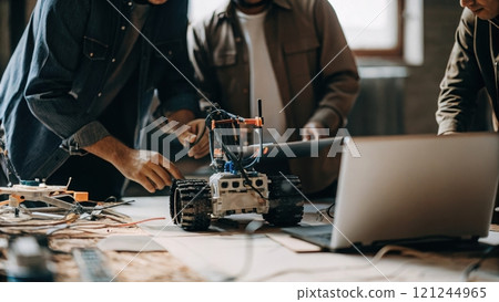 A group of individuals collaborates on assembling a robotic vehicle, technology in a creative workspace. 121244965