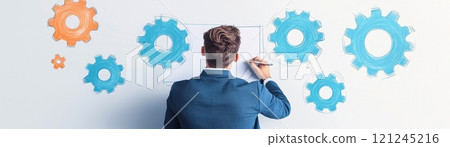A professional man is drawing colorful gears on a wall, innovation and strategic planning. A professional man is drawing colorful gears on a wall, innovation and strategic planning. 121245216