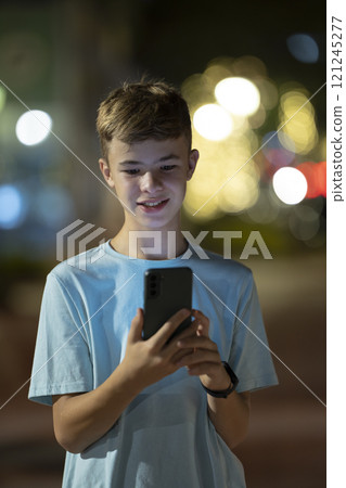 Portrait of positive happy teenager boy texting with his friend on cellphone Portrait of positive happy teenager boy texting with his friend on cellphone 121245277
