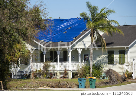 Leaking house roof covered with protective tarp sheets against rain water leaks until replacement of asphalt shingles. Damage of building rooftop as aftermath of hurricane Ian in Florida 121245563