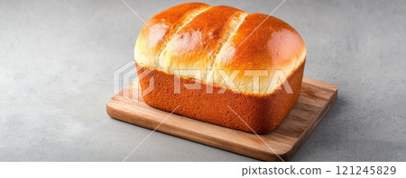 A freshly baked loaf of bread resting on a wooden cutting board 121245829