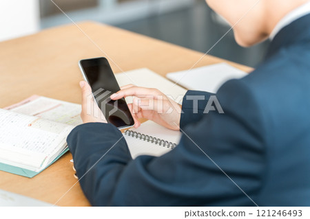 Back view of a female junior high school student sitting at a desk and using her smartphone (smartphone addiction, smartphone addiction, smartphone neck) 121246493
