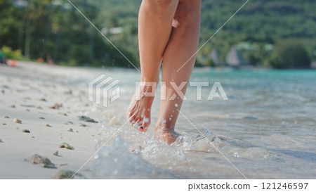 Woman walks leisurely on a tropical beach, enjoying a summer vacation. The serene setting offers a peaceful escape to relax amidst nature. Sun shining, she savors freedom and happiness by the sea Woman walks leisurely on a tropical beach, enjoying a summer vacation. The serene setting offers a peaceful escape to relax amidst nature. Sun shining, she savors freedom and happiness by the sea 121246597
