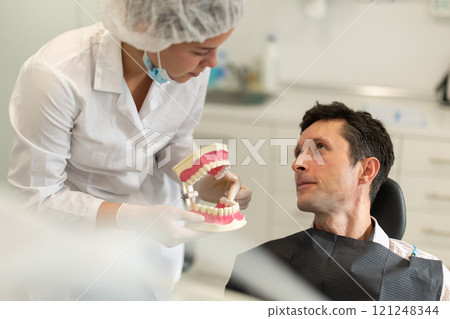 Young female dentist showing model of teeth to patient Young female dentist showing model of teeth to patient 121248344