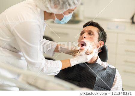 Girl doctor dentist in white coat examines oral cavity of man patient in dentistry. 121248381