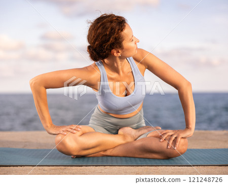 Experienced female trainer doing various exercises to warm up the body before yoga classes on seashore 121248726