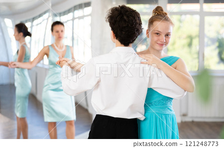Experienced female dancer teaches tango to pair of teenagers in ballroom 121248773
