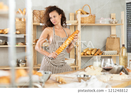 Woman in apron standing with baguette in bakery 121248812