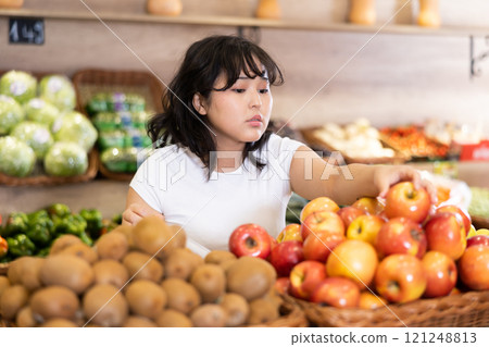 Young asian girl choosing ripe apples on store display 121248813