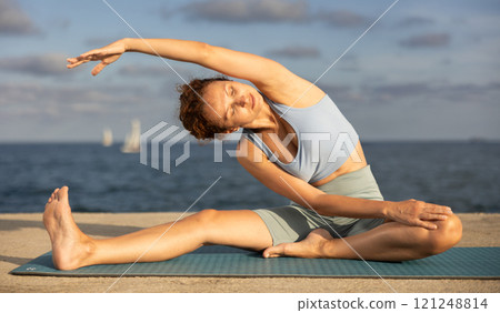 Yoga practice on embankment, female athlete fulfil carry out Janu Shirshasana Yoga practice on embankment, female athlete fulfil carry out Janu Shirshasana 121248814