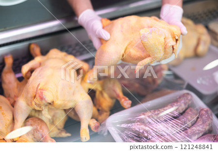 Row chicken held in hands by seller against background of showcase of butcher shop 121248841
