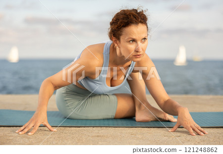 Ardha Matsyendrasana yoga pose - woman doing yoga On beach 121248862