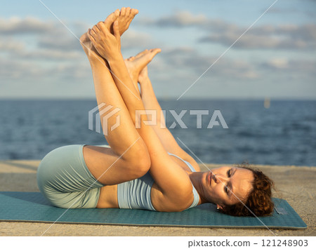 Female yoga instructor in Matyasana pose on ocean shore Female yoga instructor in Matyasana pose on ocean shore 121248903