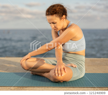 Experienced female trainer doing various exercises to warm up the body before yoga classes on seashore 121248909
