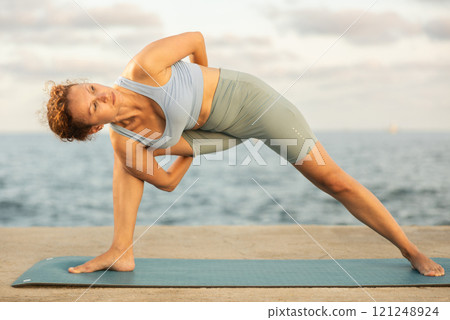 Yoga practice on embankment, female athlete fulfil carry out Parivritta Parshvakonasana 121248924