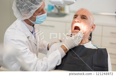 Man doctor dentist in white coat examines oral cavity of mature male patient in dentistry. Man doctor dentist in white coat examines oral cavity of mature male patient in dentistry. 121248972