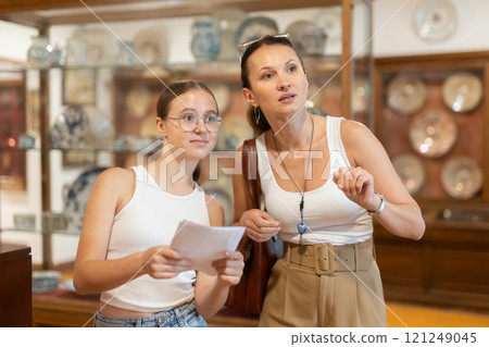 Young woman with teen daughter walk around museum, cookware zone. Young woman with teen daughter walk around museum, cookware zone. 121249045