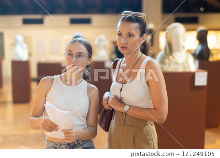 Young woman with teen daughter walk around museum, view sculpture in museum hall 121249105