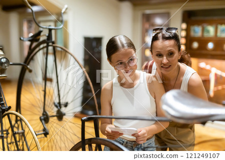 Woman and teenage girl looking at vintage bicycles in museum 121249107