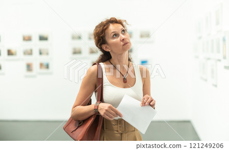 Middle-aged woman looking at pictures on wall in museum 121249206