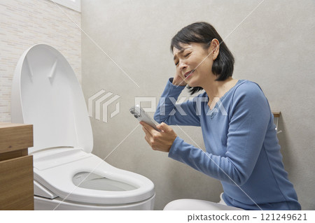 一位女士在浴室裡用智慧型手機搜尋維修公司 121249621