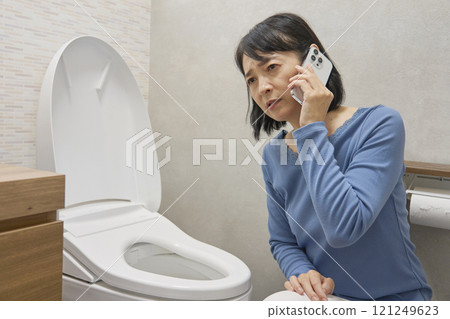 A woman calling a repairman in the bathroom 121249623