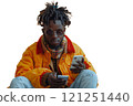 A man in a yellow jacket sits on the ground and looks at his phone 121251440