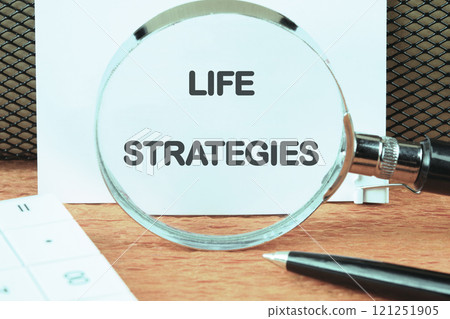 Business and technology concept. The conceptual phrase LIFE STRATEGIES on a white sheet through a magnifying glass, front view 121251905