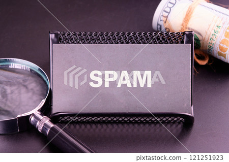Business card holder labeled spam placed next to a magnifying glass and rolled dollar bills 121251923
