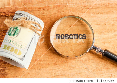 The concept of technology and development. Phrase, words, text ROBOTICS through a magnifying glass on an antique background, top view 121252056