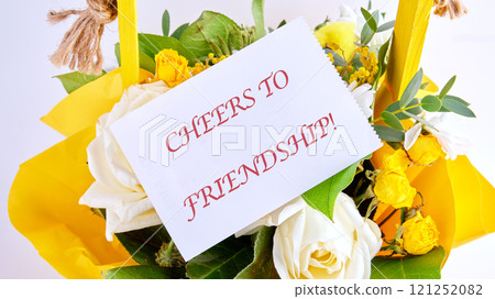 The conceptual phrase CHEERS TO FRIENDSHIP on a white card in a bouquet of flowers close-up 121252082