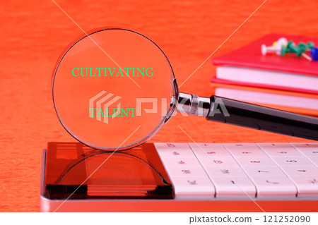 The concept of technology and business development. The concept phrase CULTIVATING TALENT written through a magnifying glass in front of an orange background, front view The concept of technology and business development. The concept phrase CULTIVATING TALENT written through a magnifying glass in front of an orange background, front view 121252090