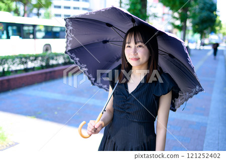 一個女人撐著陽傘在城市裡行走 一個女人撐著陽傘在城市裡行走 121252402