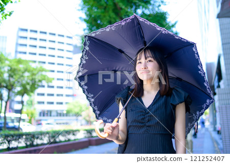 一個女人撐著陽傘在城市裡行走 121252407