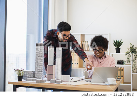 Indian man and African woman collaborate on architectural model in modern office setting. Creative teamwork atmosphere with bright natural light and focus on innovative urban design concepts. Indian man and African woman collaborate on architectural model in modern office setting. Creative teamwork atmosphere with bright natural light and focus on innovative urban design concepts. 121252998