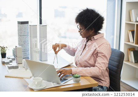 African woman architect uses compass to design modern city project in office. Shows focus, creativity, professional skill. Captures dynamic working environment in architectural design. 121253014