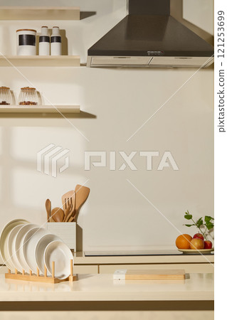 Close-up of kitchen counter for presenting products; white and beige modern kitchen background for commercial picture concept. Fresh fruit, ceramic plates, a cutting board, and wooden cooking tools. 121253699