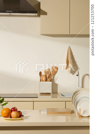 A front of a beige modern kitchen background for a commercial photo concept; kitchen table for displaying the product. Wooden kitchen equipment, a cutting board, porcelain plates, and fresh fruit. 121253700