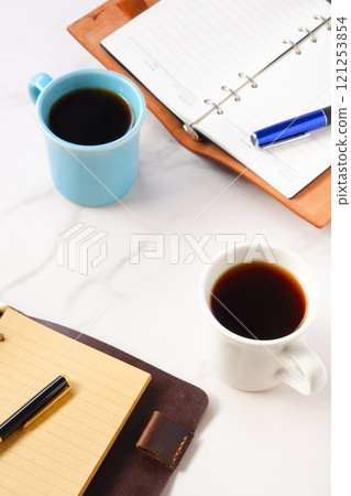 An image of two people having a meeting while drinking coffee, with two mugs of coffee and a system notebook An image of two people having a meeting while drinking coffee, with two mugs of coffee and a system notebook 121253854