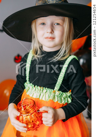 Children's Halloween - a girl in a witch hat and a carnival costume with airy orange and black balloons at home. Ready to celebrate Halloween Children's Halloween - a girl in a witch hat and a carnival costume with airy orange and black balloons at home. Ready to celebrate Halloween 121254654