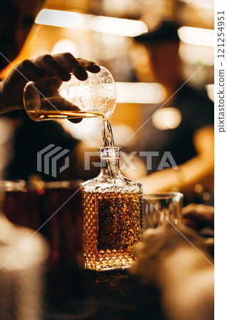 A bartender pours whiskey from a measuring glass into a decanter A bartender pours whiskey from a measuring glass into a decanter 121254951