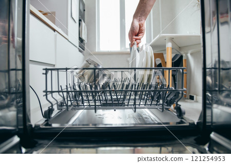 Male hand putting dirty plate in dishwasher, view from inside dishwasher. Household chores, man washing dishes 121254953