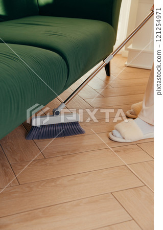 Dry cleaning the floor under furniture with a long-handled brush Dry cleaning the floor under furniture with a long-handled brush 121254971